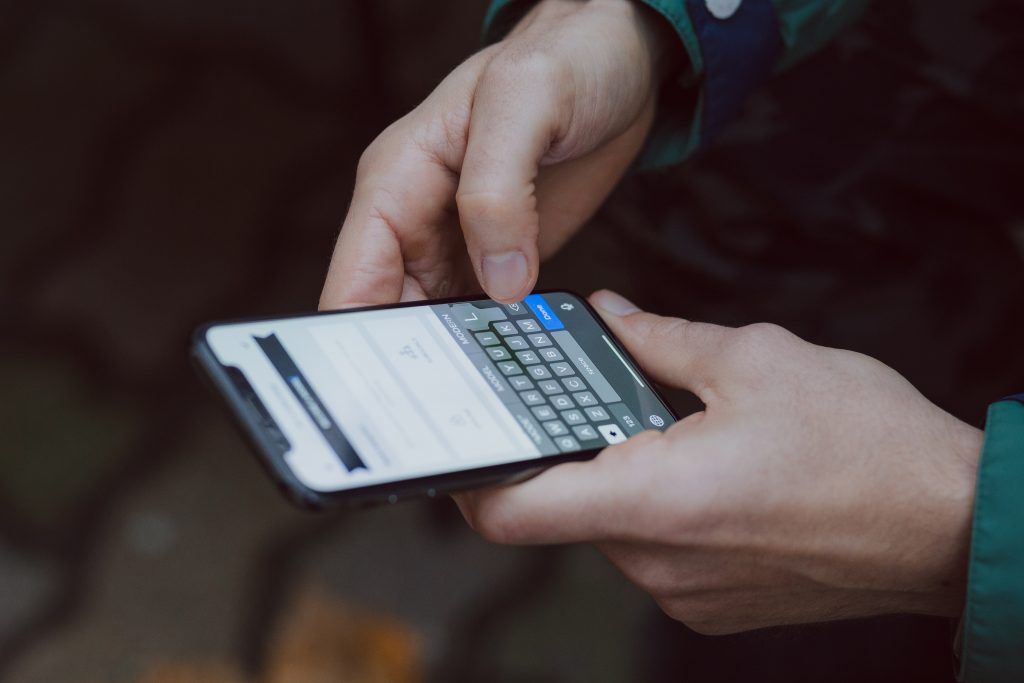 A close up picture of a person's hands holding a smartphone typing on the keyboard.